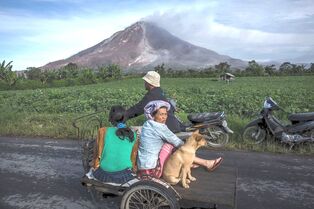 Three people with a dog on a motorbike in front of a volcano in Sumatra